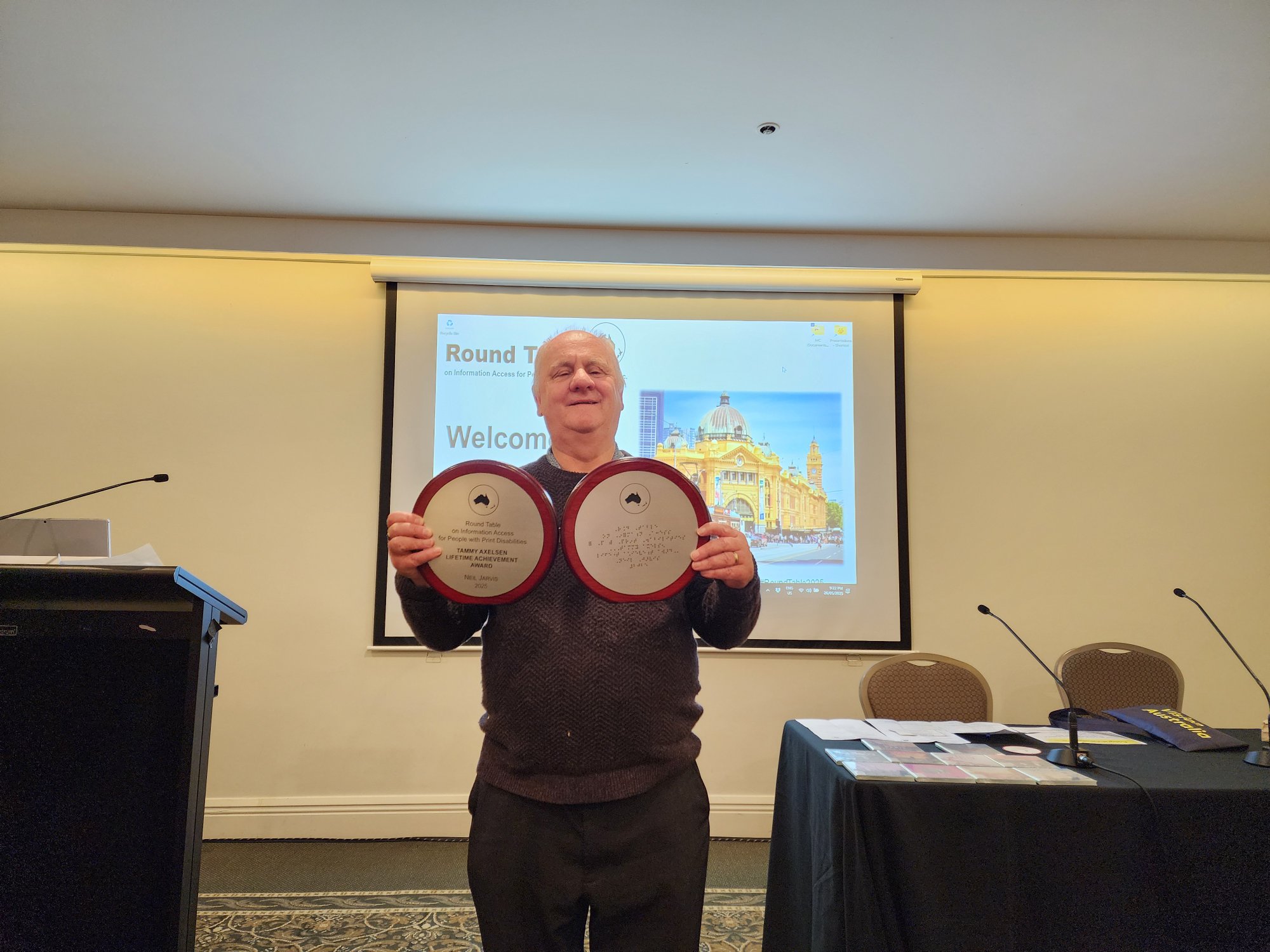 Neil Jarvis holding two circular awards at the Round Table conference in Melbourne
